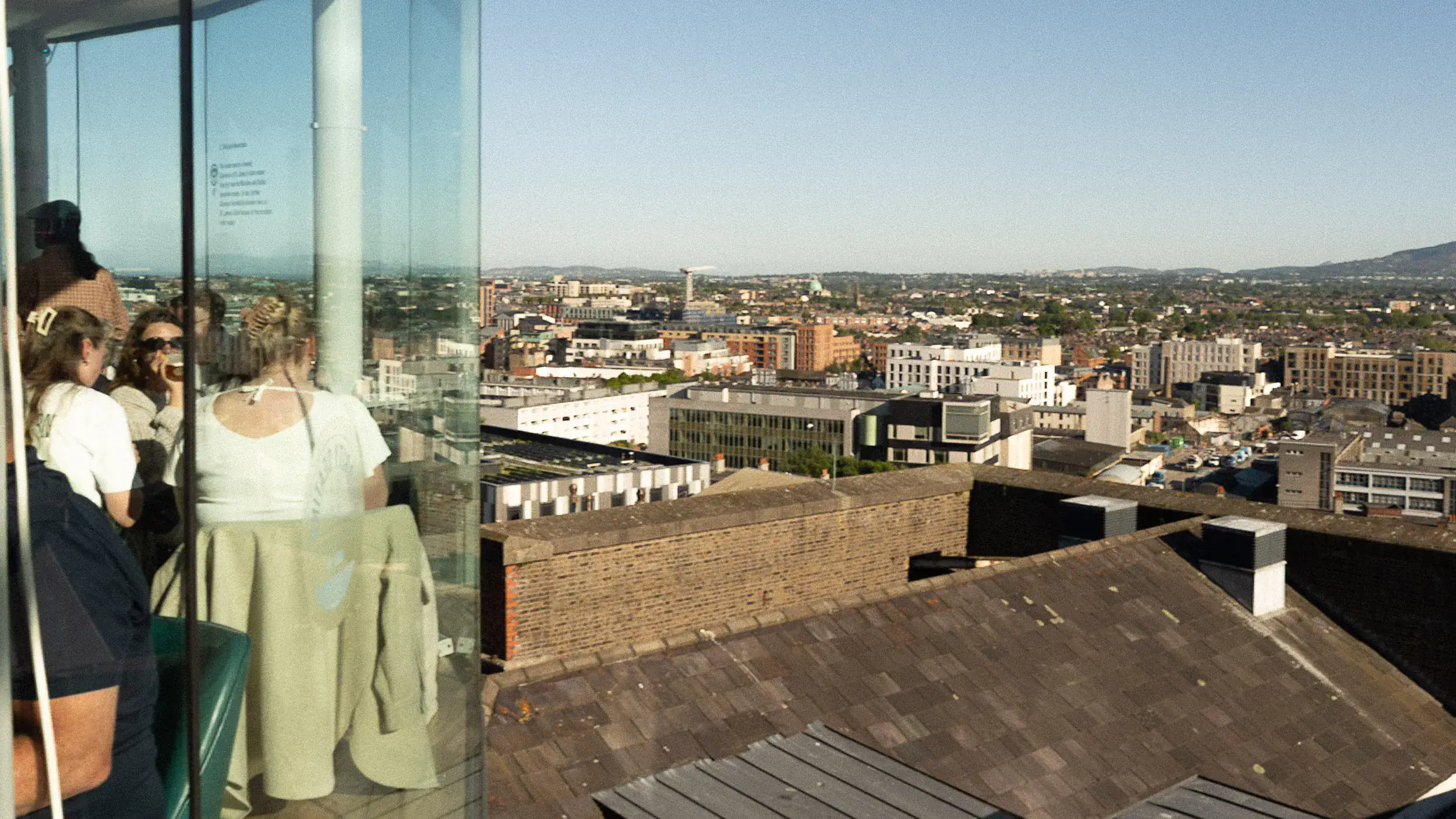 View from inside the Gravity Bar at the Guinness Storehouse in Dublin. Visitors sip pints of Guinness near the curved glass windows, overlooking the city skyline from above.