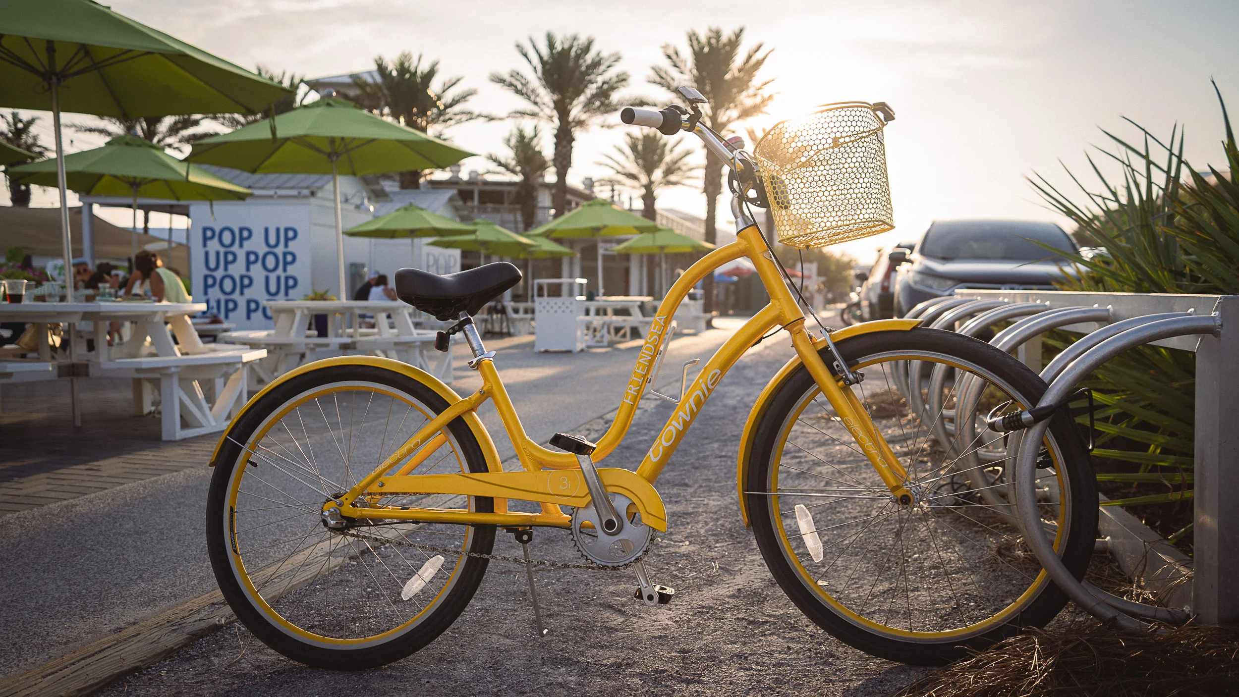Vintage yellow bicycle in Seaside with palm trees and shops in the background at golden hour.