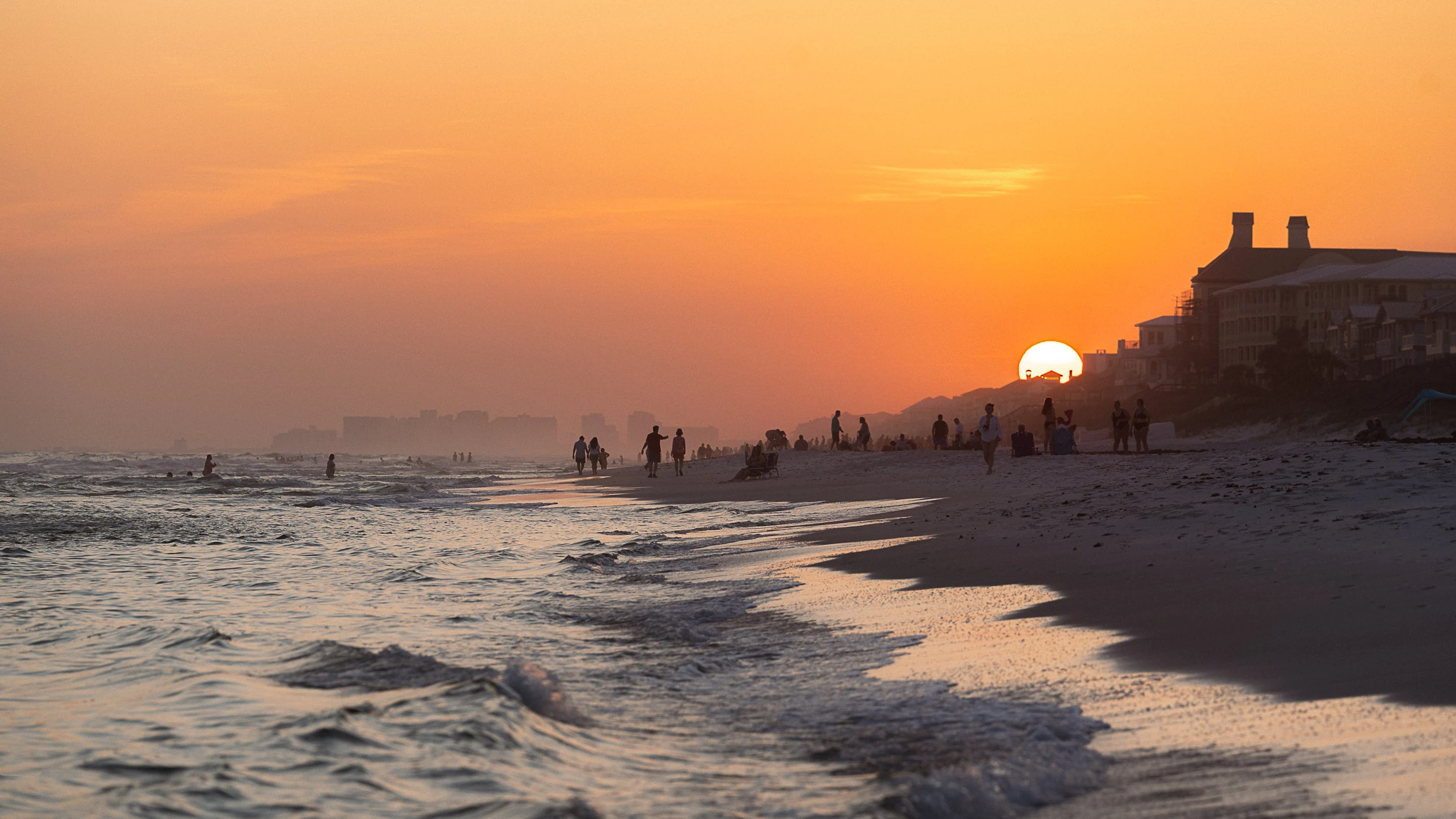 Golden sunset over Santa Rosa Beach with silhouettes of people enjoying the shoreline along Florida’s 30A coast.