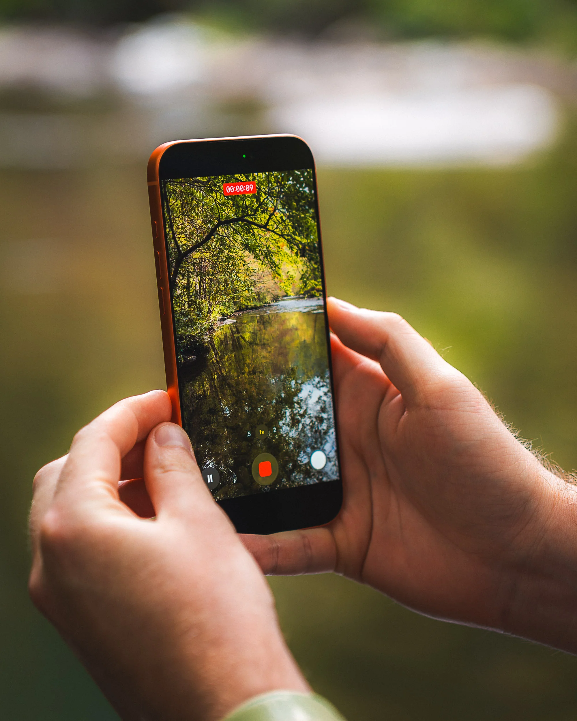 Photographer using iPhone 17 to record a video of a stream, demonstrating high-performance camera and video quality.