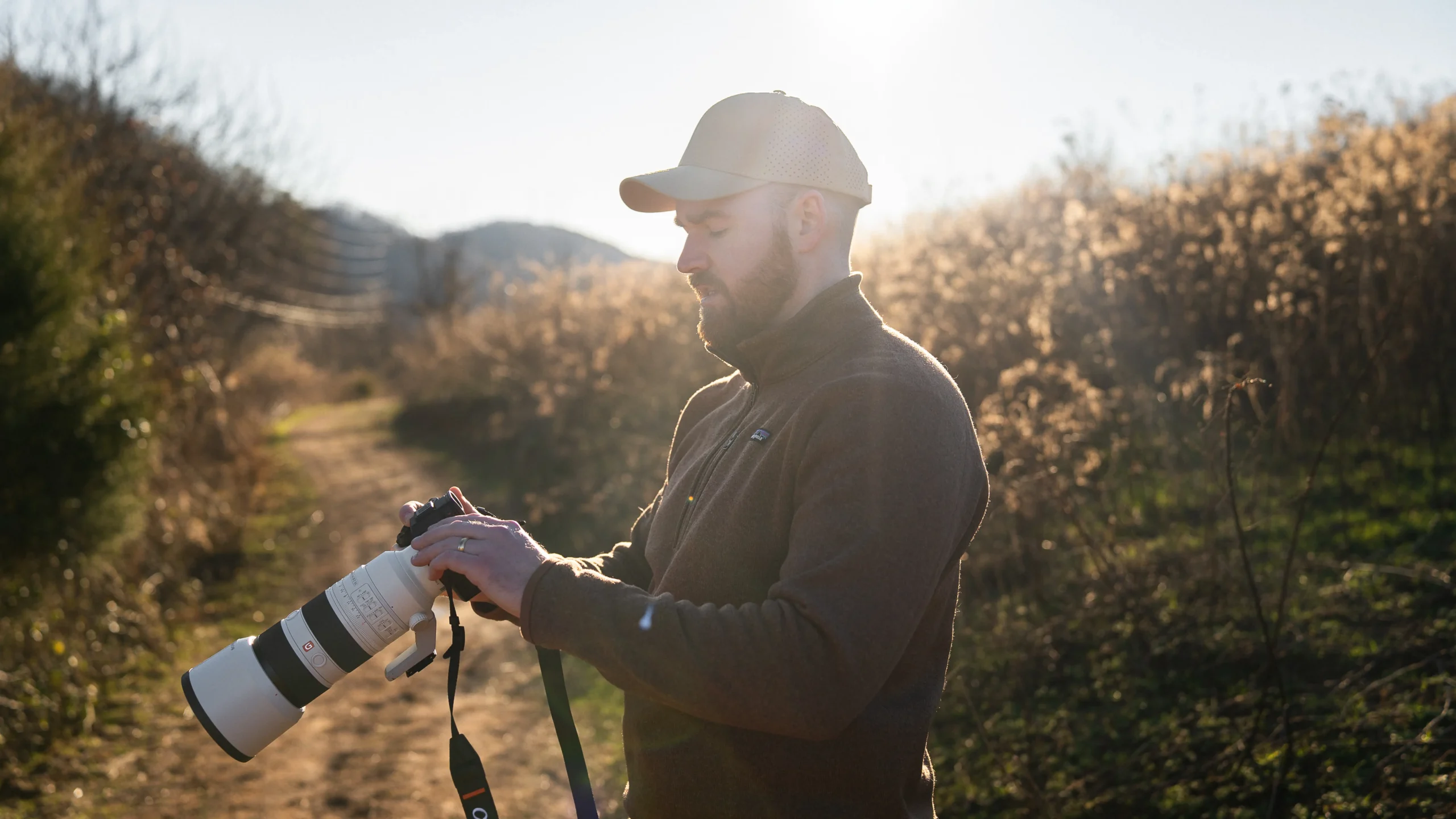 Outdoor photographer adjusting settings on the Sony A7 V camera at sunset with sun flare in the background