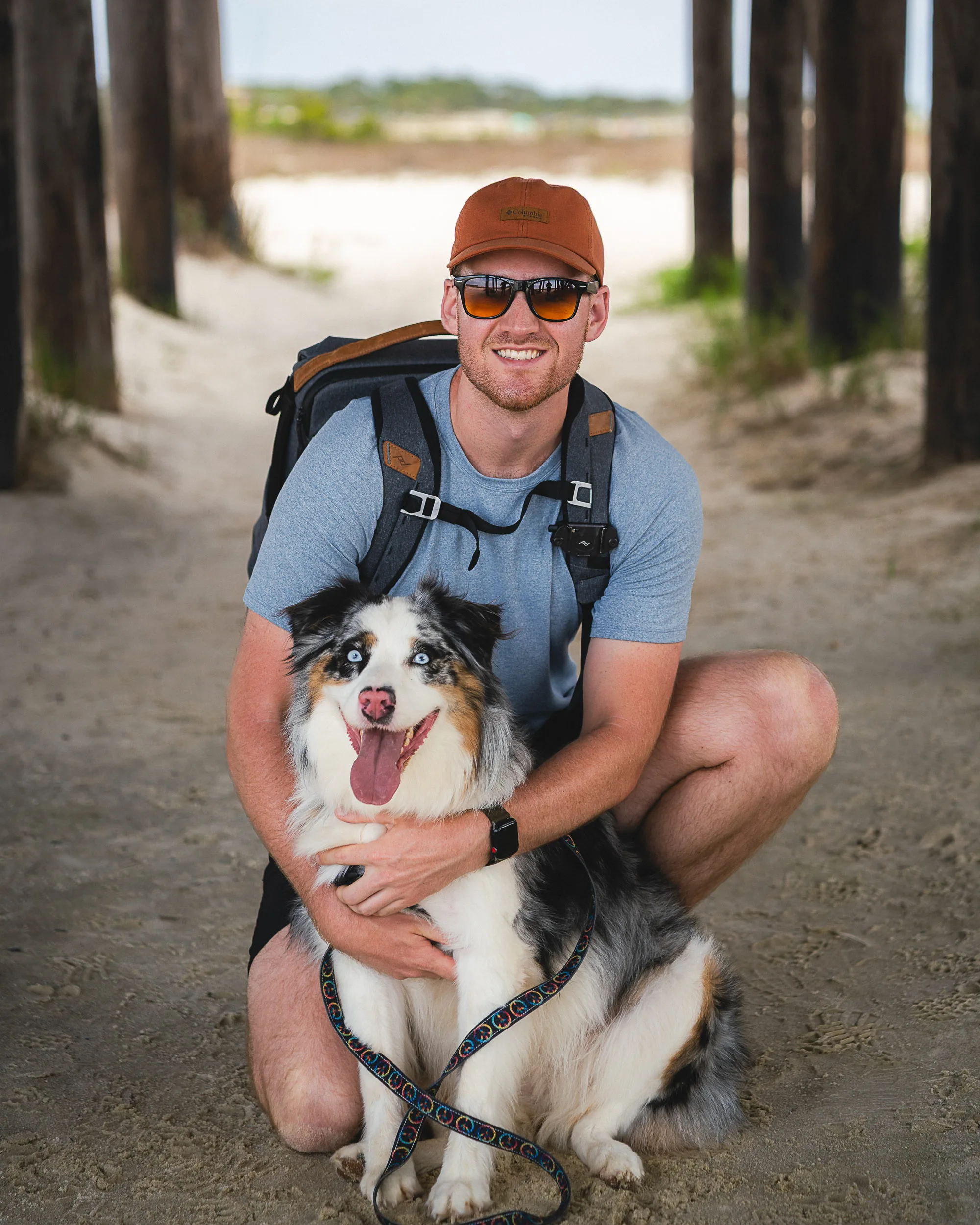 Beach portrait with dog, kneeling down with an Australian Shepherd smiling at the camera